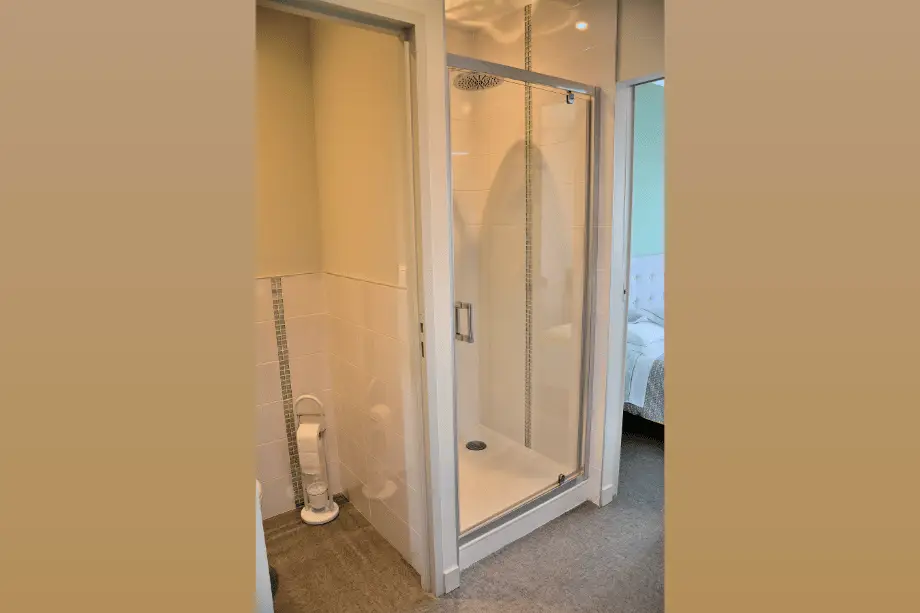 Douche de la suite Watermael avec WC séparé et chambre visible à l’arrière-plan