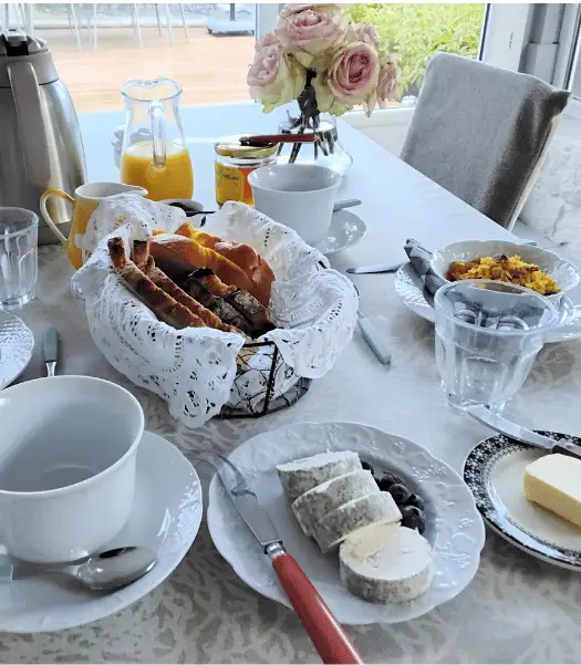 Petit-déjeuner servi à table avec pains, jus d’orange, boissons chaudes, fromages et fleurs